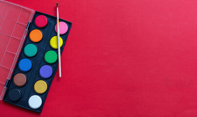 Creative kids, painting and drawing. Colorful paints and brush on red color background, empty...