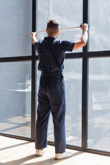 back view of workman in overalls measuring large windows