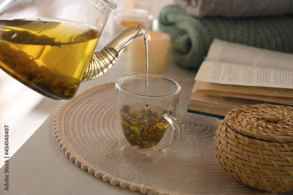 Poster Pouring freshly brewed tea into cup at table in room, closeup. Cozy home atmosphere