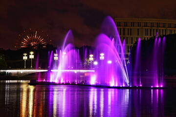 Colorful purple fountains on Svisloch River on the Ferris wheel background in the Yanka Kupala Park at summer night, a beautiful view of Minsk , a famous national landmark of the capital of Belarus