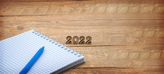 Notebook and pen on the table. A blank sheet of paper and a ballpoint pen. Wooden numbers 2022.