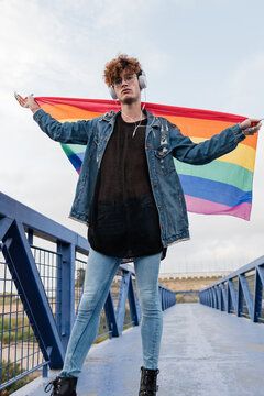 Gay man with rainbow flag listening to music in headphones