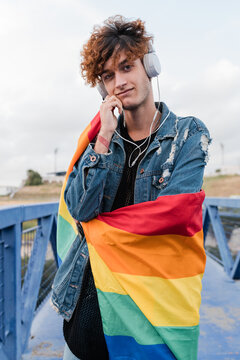 Gay man with rainbow flag listening to music in headphones