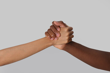 Woman and African American man clasping hands on light grey background, closeup