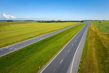 Fototapeta premium Asphalt highway through green summer field. Aerial view