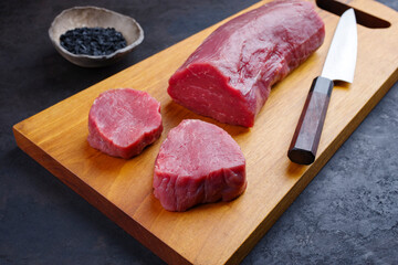 Traditionelles rohes Rinderfilet Steak Natur mit schwarzem Salz als close-up auf einem Modern Design Holz Board 