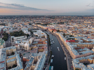 Fototapeta na wymiar Sunset aerial view on Fontanka river and old houses in center of St Petersburg. Colorful rooftops. Boats float on the water. Russia in the summer. Place for vacation. Nevsky prospect on background.