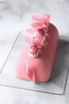 Contemporary Ruby Chocolate, Red Currant and Matcha Yule Log Mousse Cake covered with ruby chocolate velvet spray and decorated with ruby chocolate elements, on a gray background.