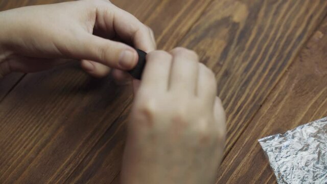 Human hands twist brown ribbon into roll on wooden table, then pack it in small sealed bag and take two more bags with other tapes. Packaging of materials for handmade. Crafter's workshop.
