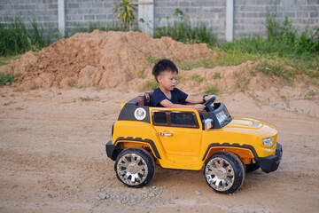 Fototapeta na wymiar Cute Asian kid driving electric toy car auto home backyard on nature in summer. Outdoor toys, Little 5 years old kindergarten schoolboy in Battery-powered Ride-on Car vehicle