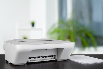 Compact laser printer on black desk against blurred background