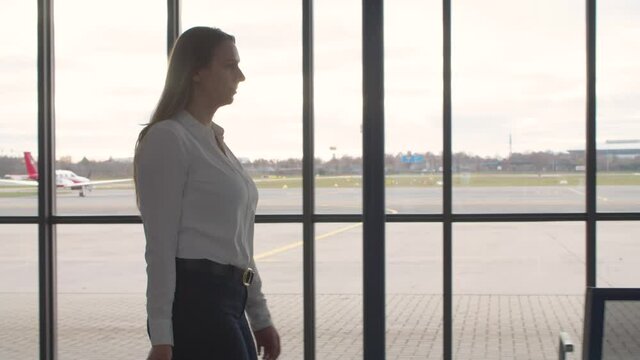 young business woman from the side in an airport with a suitcase walking to privat jet