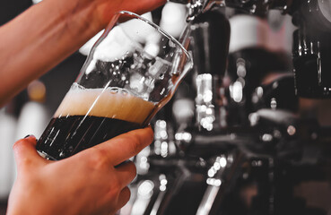 woman's hand holds a glass and pours dark foamy beer from the tap
