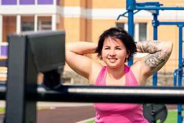 young woman shakes her back muscles in the city yard using street exercise machine hyper extension...