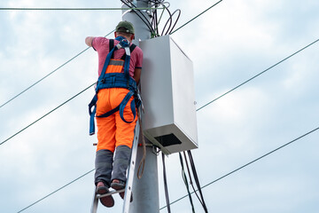 electrician or telecommunications lineman works on laying a cable at the top of a telephone pole