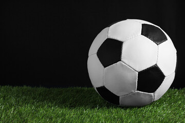 Fototapeta na wymiar Football ball on green grass against black background. Space for text