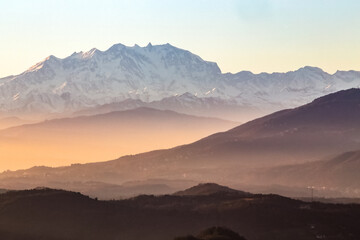 View of the misty and fog surrounding the mountains of the Italian Alps at winter sunset.  Layers of mountains. Nature tourism.