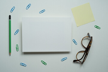 desk, white card, rectangle, space for text, design, green pencil, reminder, yellow card, brown glasses, paper clips, on a white background, photo from above