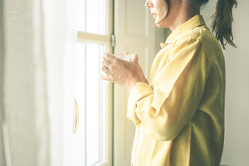 Young woman drinking a cup of tea looking outside the window Portrait of a girl enjoying free time at home. Middle aged female with a drink in the hand look through the door. Lifestyle leisure concept