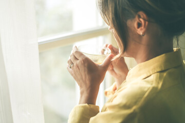 Young woman drinking a cup of tea looking outside the window Portrait of a girl enjoying free time at home. Middle aged female with a drink in the hand look through the door. Lifestyle leisure concept