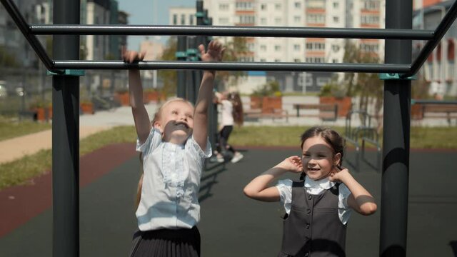 Two little schoolgirls jumping onto the monkey bars at a playground in schoolyard. Schoolmates wearing school uniform and play during school break.