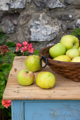 Top view of basket with green apples from orchard on rustic wooden table, stone wall background, vertical
