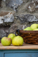 View of basket with green apples, freshly picked, on rustic wooden table, stone wall background, vertical, with copy space