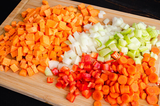 Chopped Vegetables On A Bamboo Cutting Board: Peeled And Diced Sweet Potatoes, Onion, Celery, Carrots, And Red Bell Pepper On A Wood Cutting Board