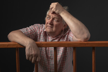 Man in sixties on trial, standing behind wooden dock with fearful facial expression 