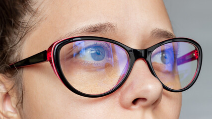 Close up of woman's eyes with red and black female glasses for working at a computer with a blue filter lenses on a gray background. Anti blue light and rays. Eye protection