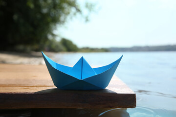 Light blue paper boat on wooden pier near river