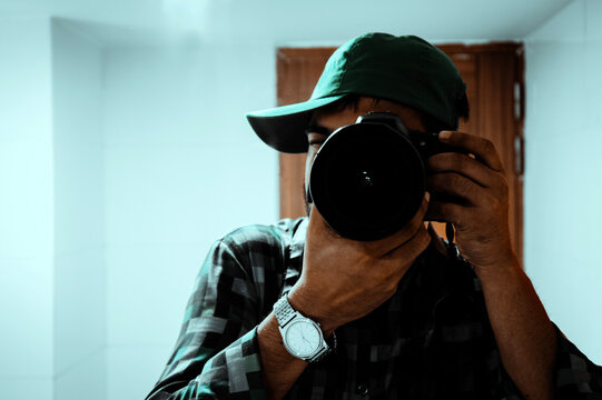 Young man taking photos with dslr camera inside the room. Man clicking pictures with a professional camera indoors. 