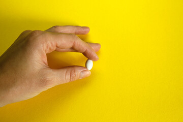 female hand holding white pill  over yellow background