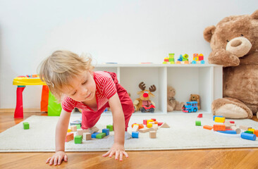 Sweet happy child boy having fun at home playing with his giant teddy bear and colorful wooden blocks and toys, on the floor.