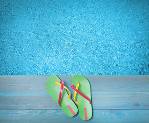 Pair of flip flops on wooden deck near swimming pool, top view