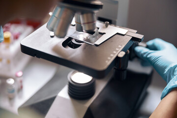 Woman lab assistant adjusts microscope with sample on slide in laboratory closeup