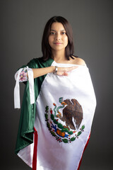 Beautiful young Mexican woman saluting the flag of Mexico in grey background.  Independence day in Mexico. September celebration in Mexico.
