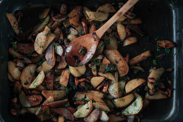 Fried potatoes with mushrooms and herbs in a pan with a wooden spoon