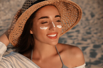 Happy young woman with sun protection cream on face at beach