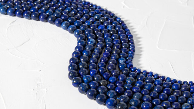 Blue necklaces made from natural lazurite  are beautifully laid out on a white surface.  Isolated lapis lazuli jewelry. Round beads. 