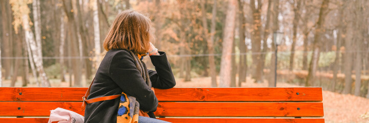 autumn time. beautiful woman traveler dressed up in fall fashion. the girl sits on a bench and looks at the autumn landscape in the park. local solo travel concept. banner