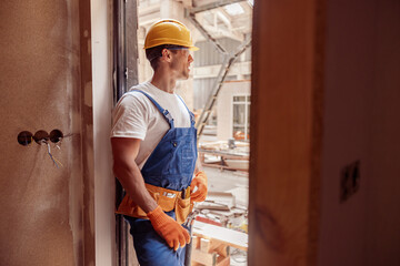 Athletic male builder in work overalls standing in doorway