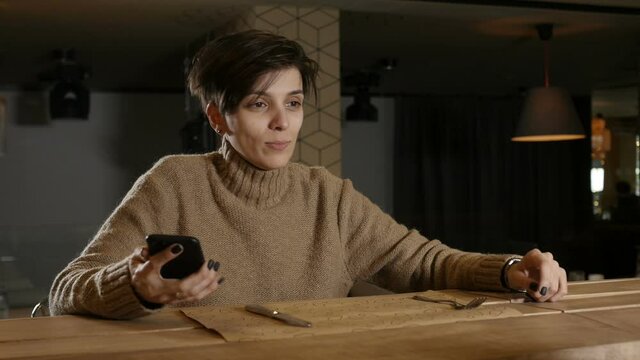 a lonely girl with a short haircut sits in a restaurant, smiles and looks at the phone. High quality FullHD footage