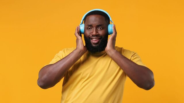 Vivid cheerful young bearded african american man 20s wears orange t-shirt listen music in headphones dance sing song fooling around have fun enjoy isolated on plain yellow background studio portrait