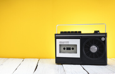 An old 1970s cassette recorder stands on a wooden table against a yellow background. 