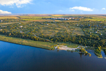 Aerial photography, the river bank against the background of sunset summer sunbeams, steppe trees and a working village in the background.