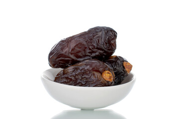 Several royal dates in a white ceramic dish, close-up, isolated on white.