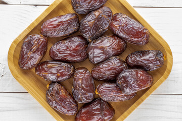 Several royal dates with a bamboo plate on a wooden table, close-up, top view.