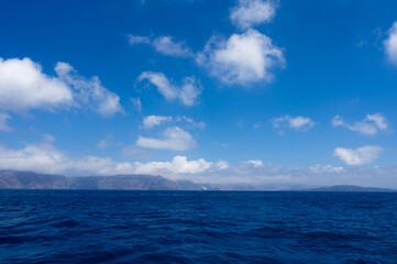 Naklejka na ściany i meble View from sea of silhouette of Santorini island, Greece. Luxury tourism. Blue cloudy sky.