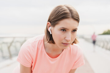 Concentrated serious young woman female jogger listening to the music favorite song soundtrack in earbuds preparing for running on city bridge.